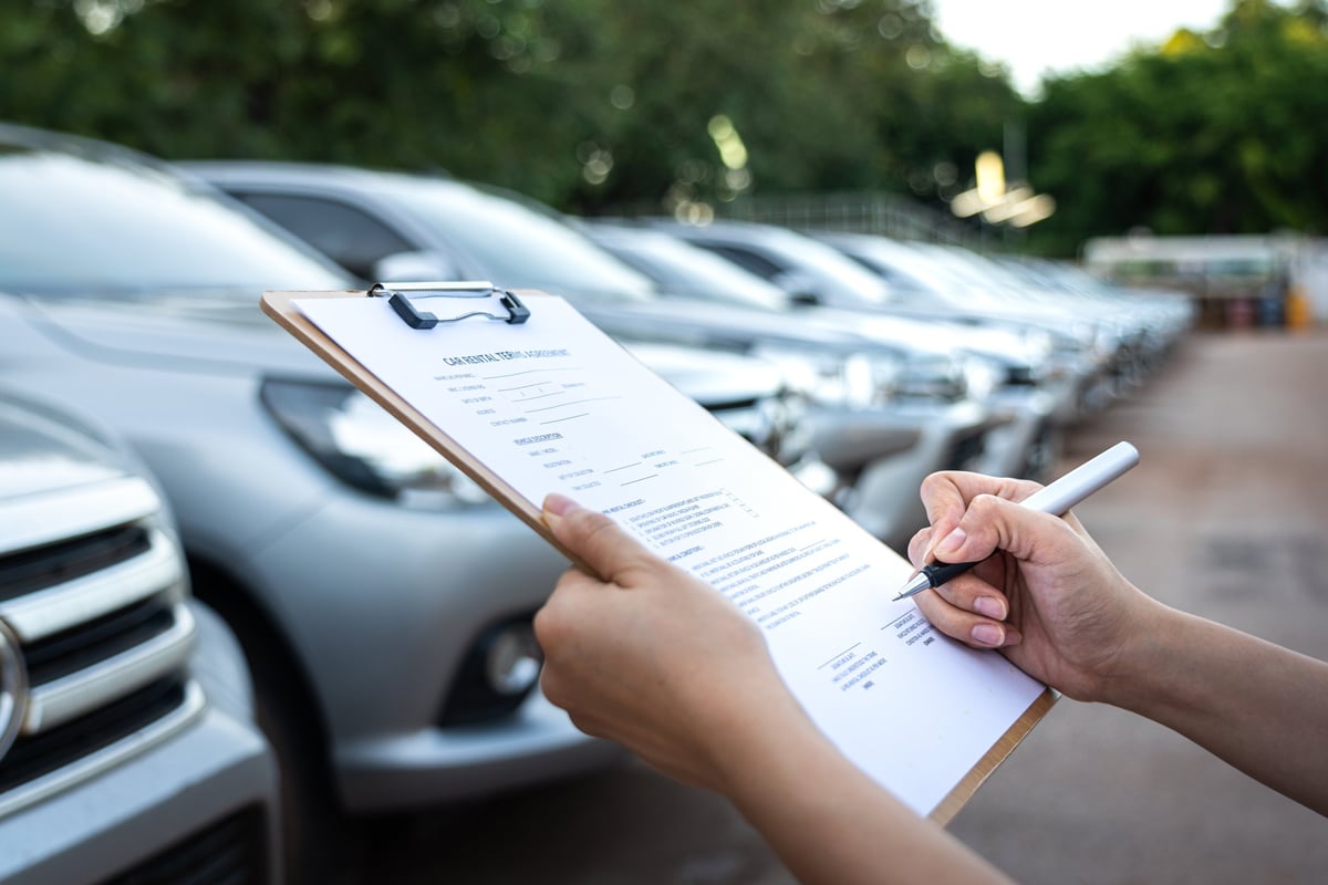 Customer signing a car rental agreement with a row of vehicles in the background